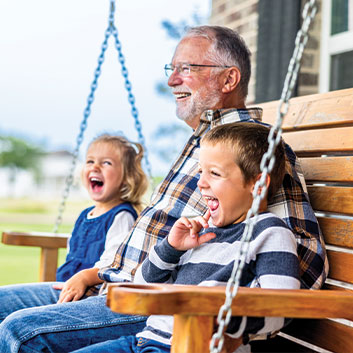 Grandfather sitting of a swinging seat with his two grandchildren laughing. Read about Gifts from Retirement Plans Grandfather sitting of a swinging seat with his two grandchildren laughing. Read about Gifts from Retirement Plans